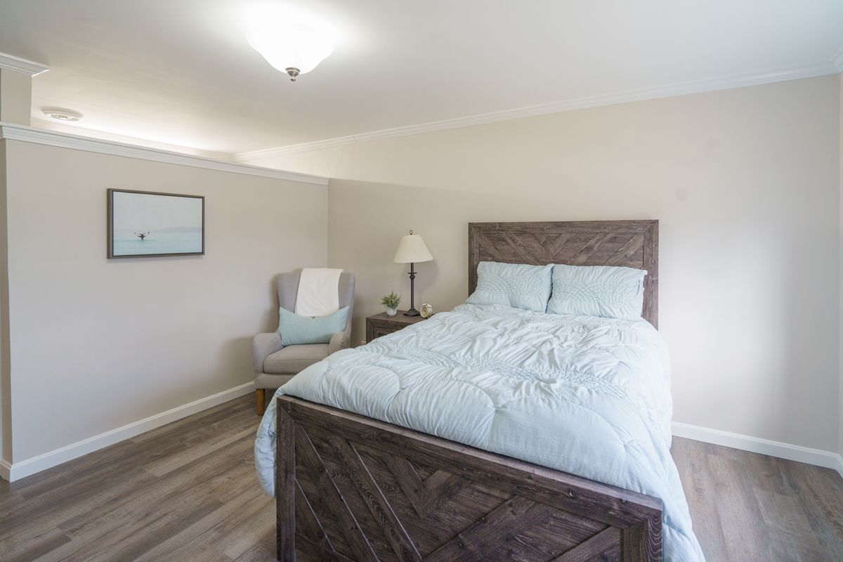 A bedroom with a bed , chair , nightstand and lamp.