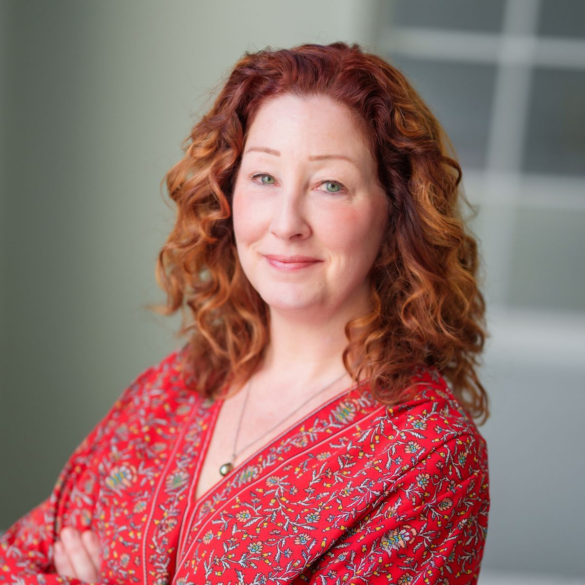 A woman with red hair is wearing a red shirt and necklace.