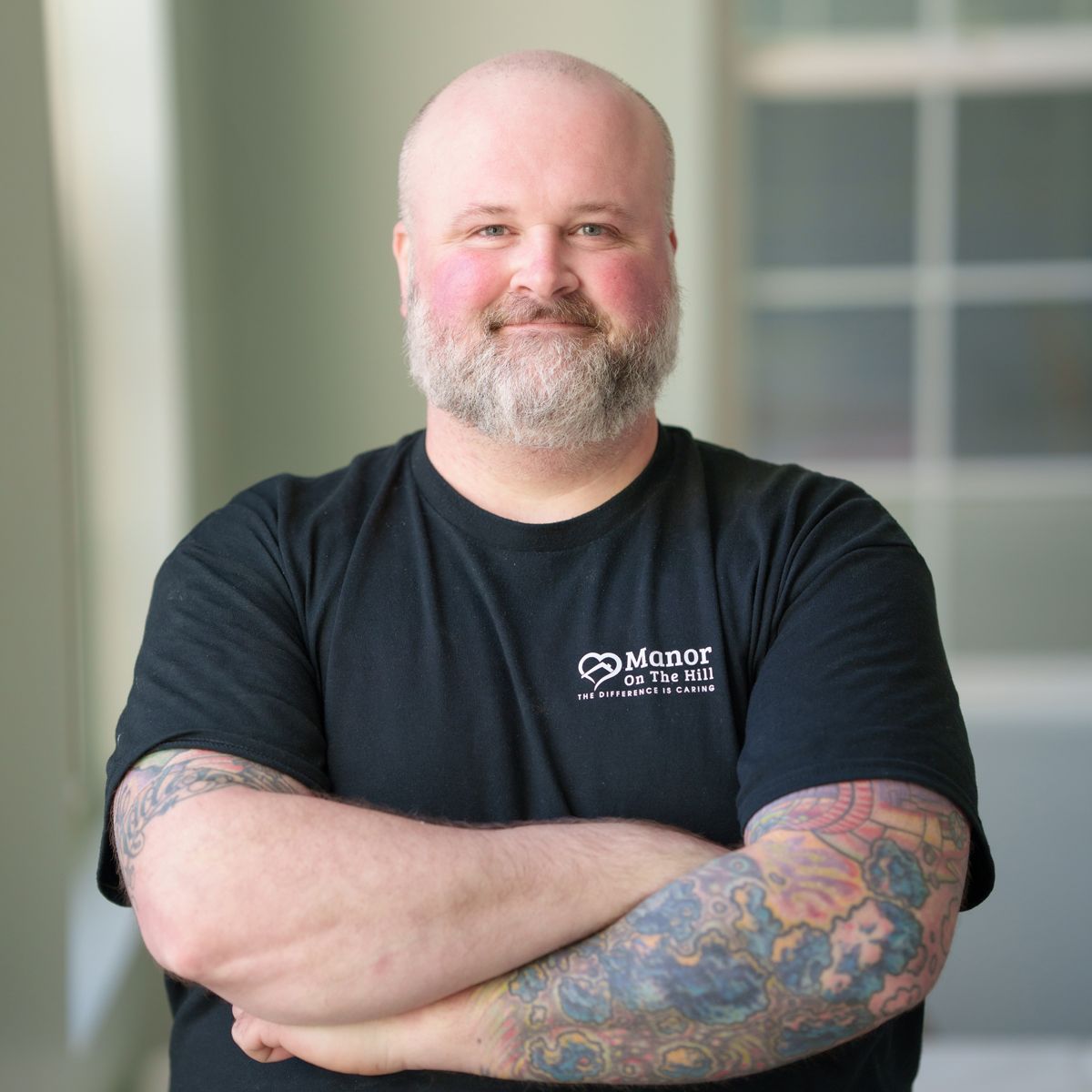 A bald man with a beard and tattoos is wearing a black shirt