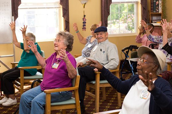 A group of elderly people are sitting in chairs with their hands in the air.