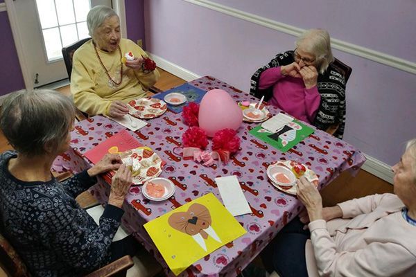 A group of elderly women are sitting around a table with plates of food