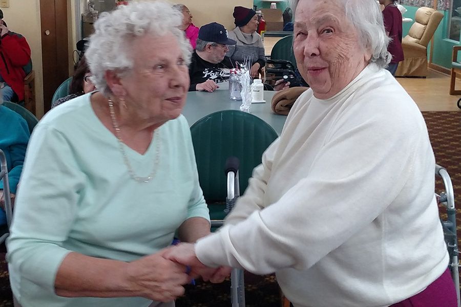 Two elderly women are shaking hands while sitting at a table