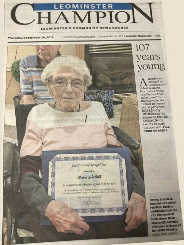 A woman in a wheelchair is holding a certificate on the front page of a leominster champion newspaper