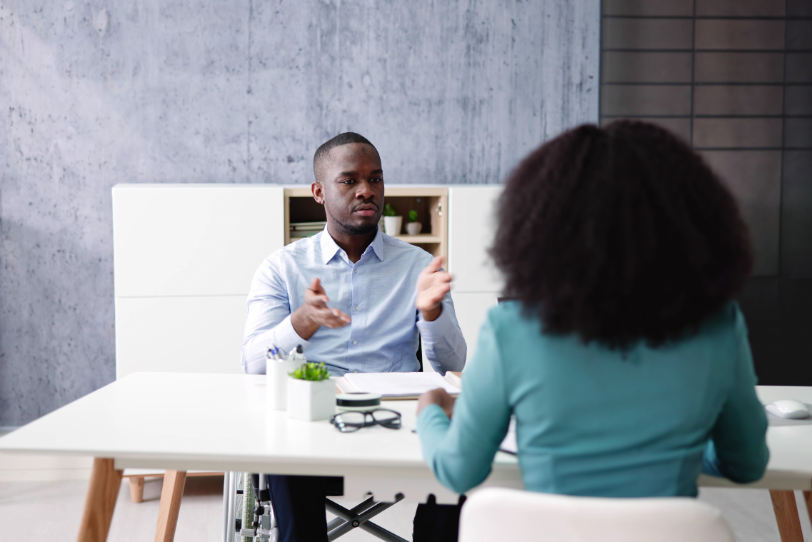 Un homme en fauteuil roulant est assis à une table et parle à une femme.