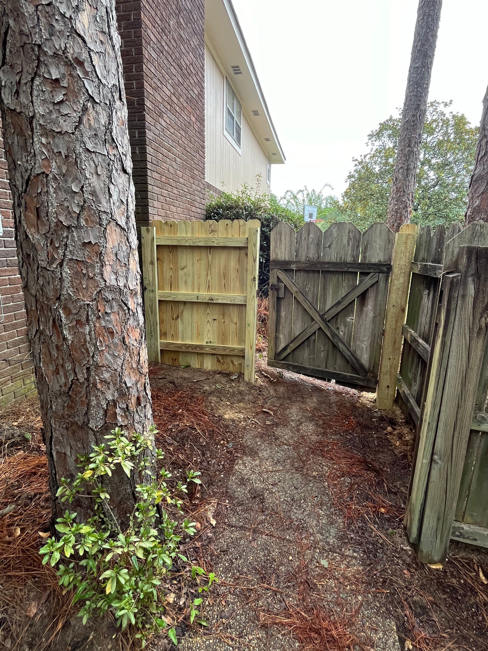 A wooden gate is between two trees next to a house.