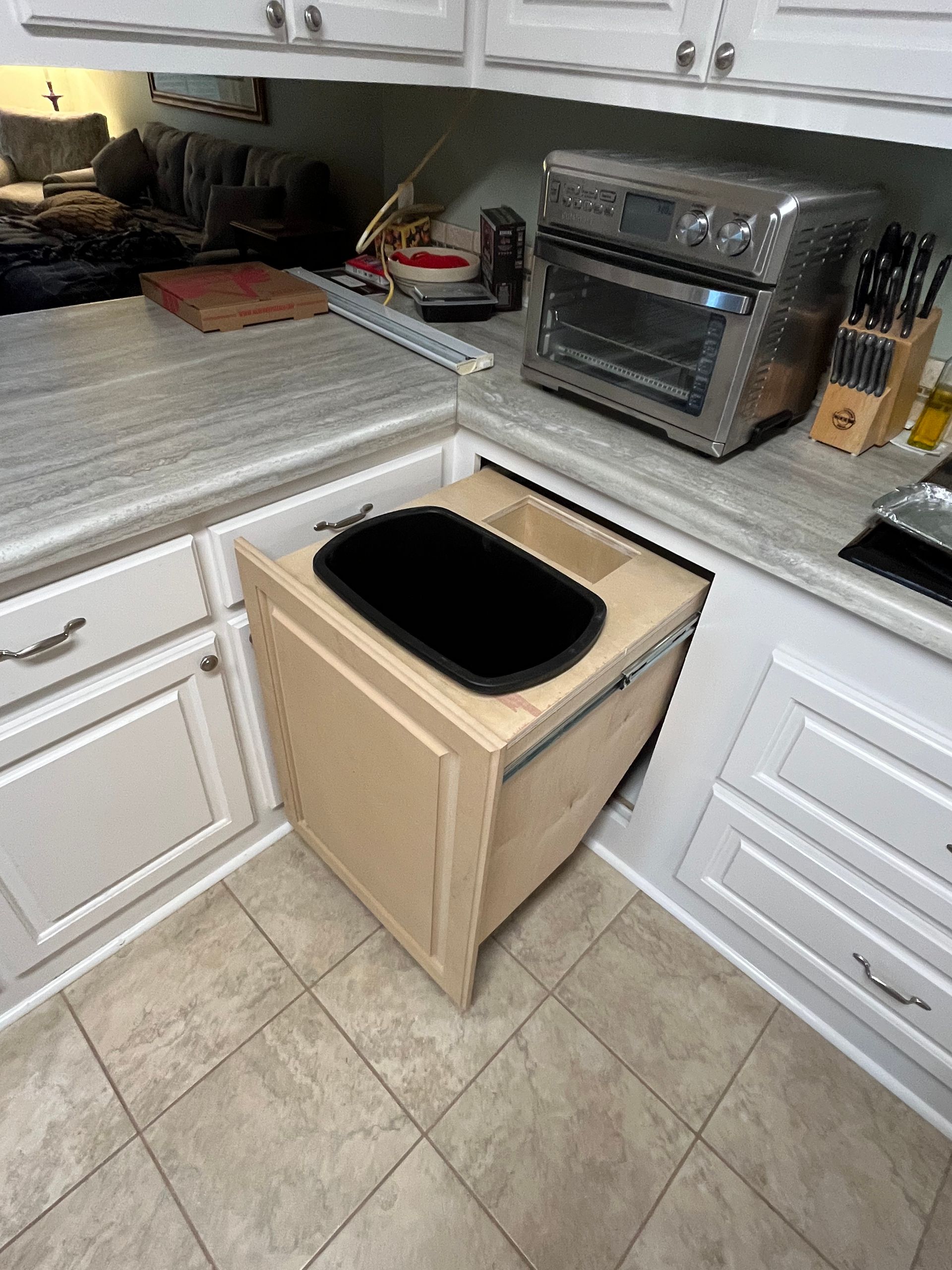 A kitchen with a trash can in the corner and a toaster oven.