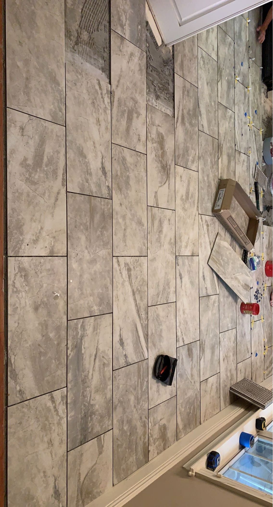 A person is laying tiles on a wall in a bathroom.