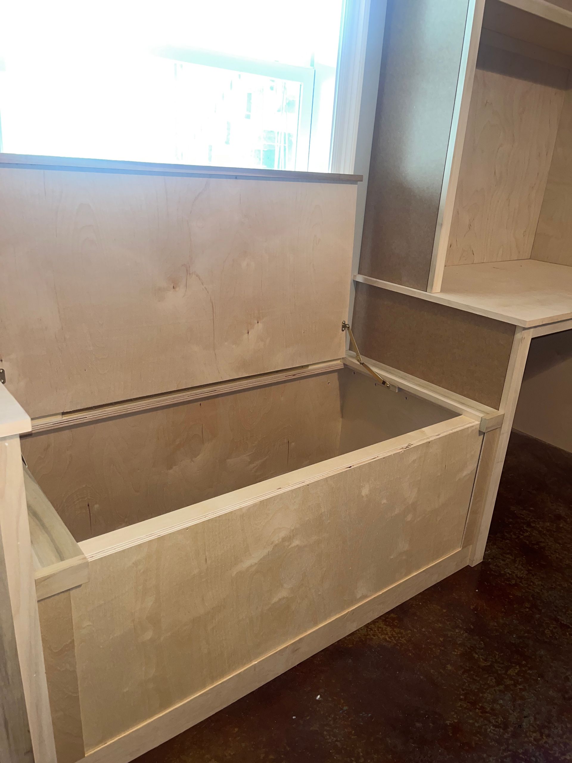 A white bench with the lid open in a room next to a window.