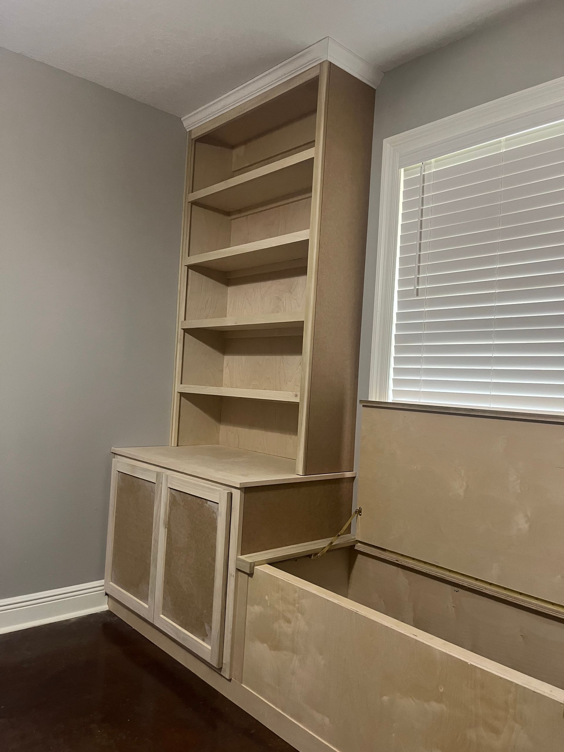 A room with a bookshelf and a window with blinds.