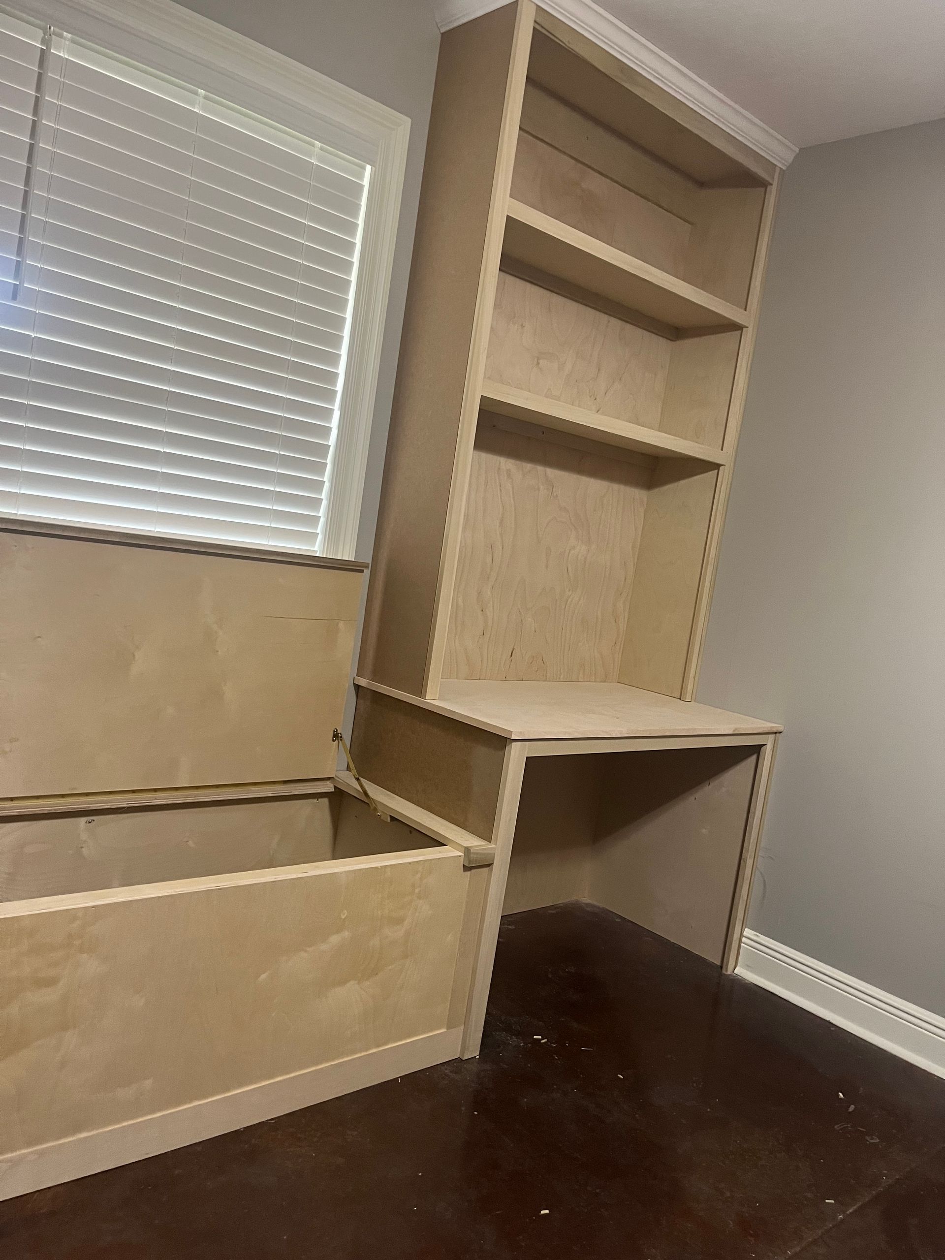 A room with a desk , shelves and a window.