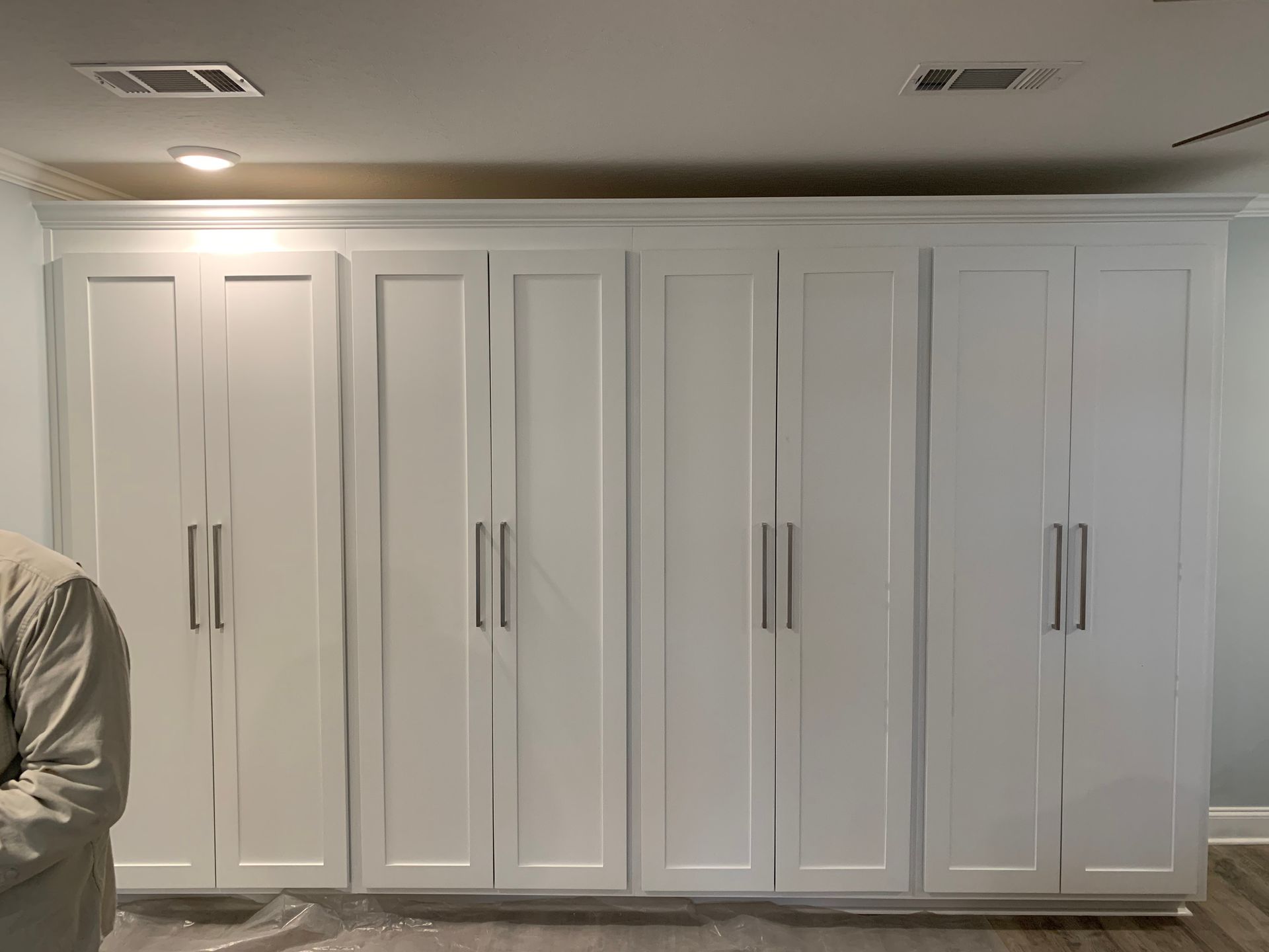 A man is standing in front of a wall of white cabinets.