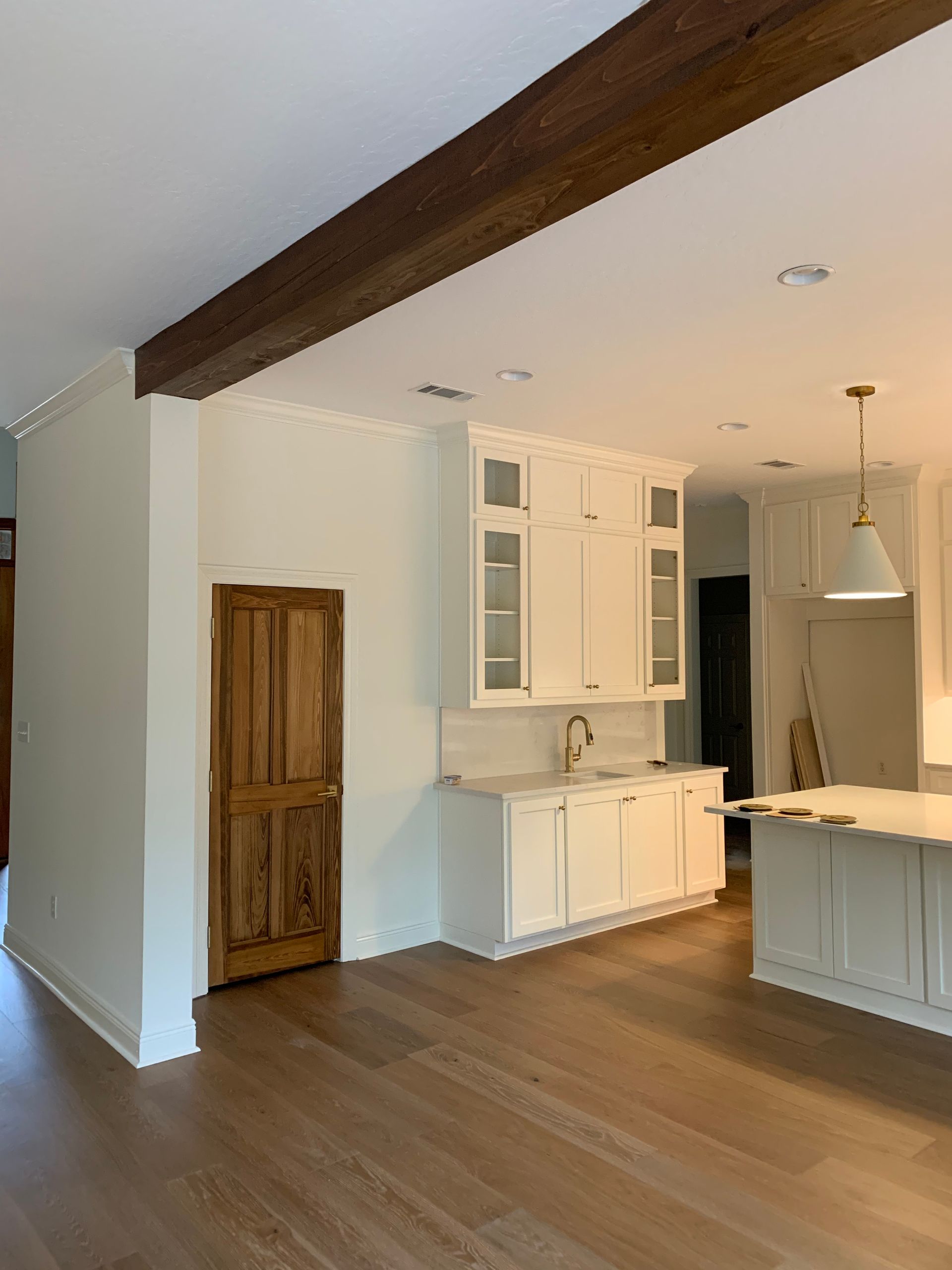 A kitchen with white cabinets , hardwood floors , and a wooden door.