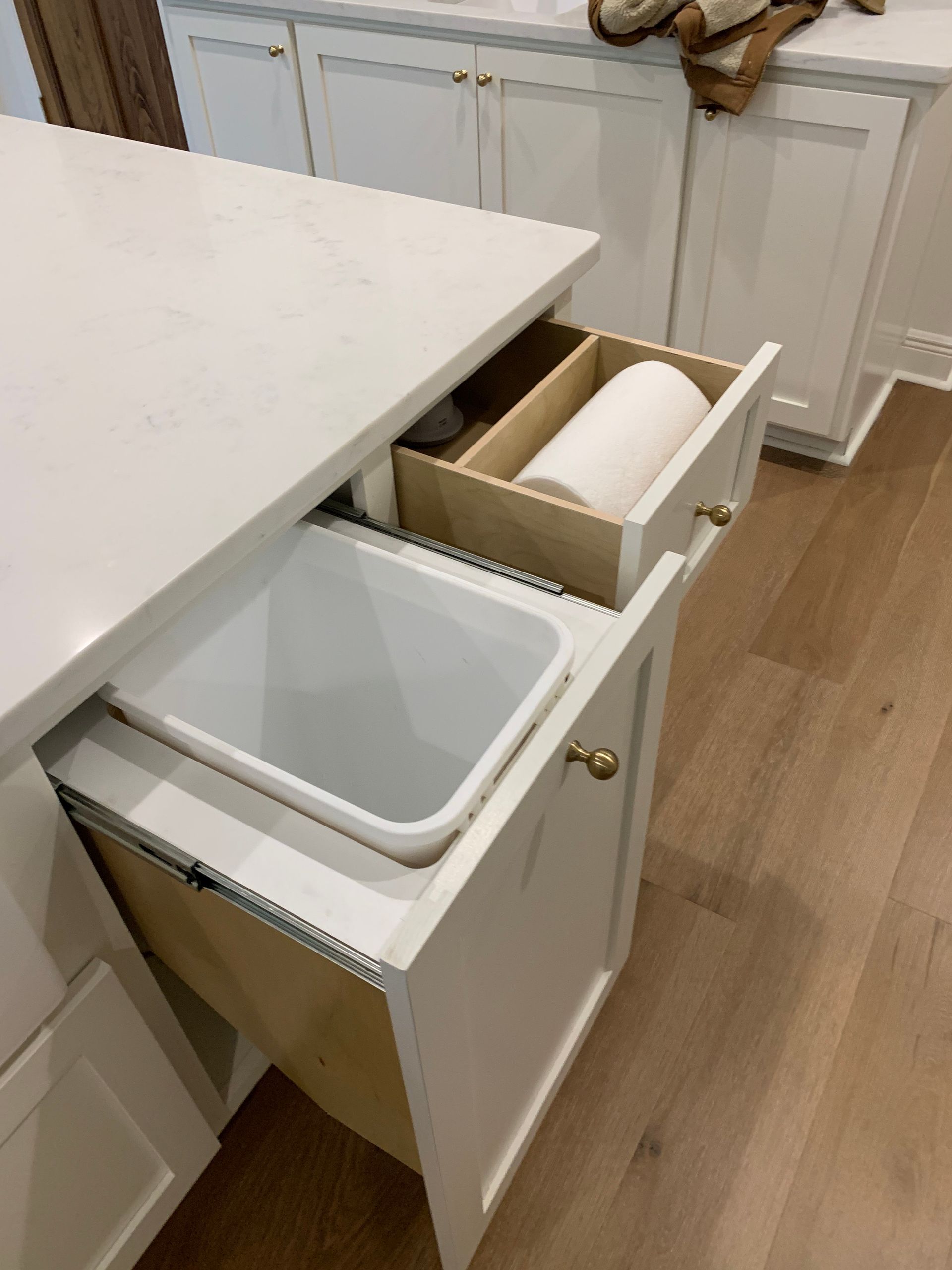 A trash can is pulled out of a drawer in a kitchen.