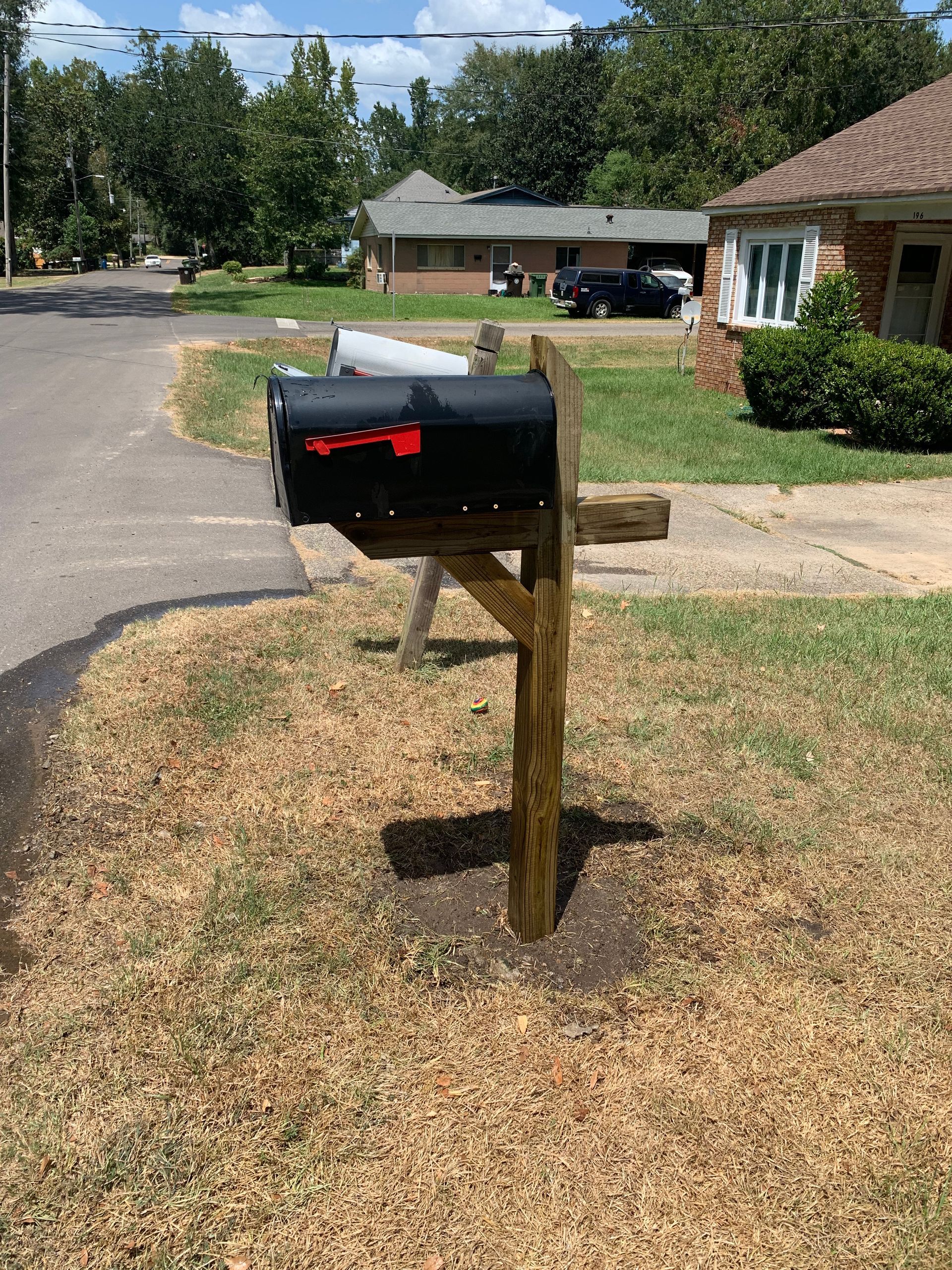 A black mailbox is sitting on a wooden post in front of a house.