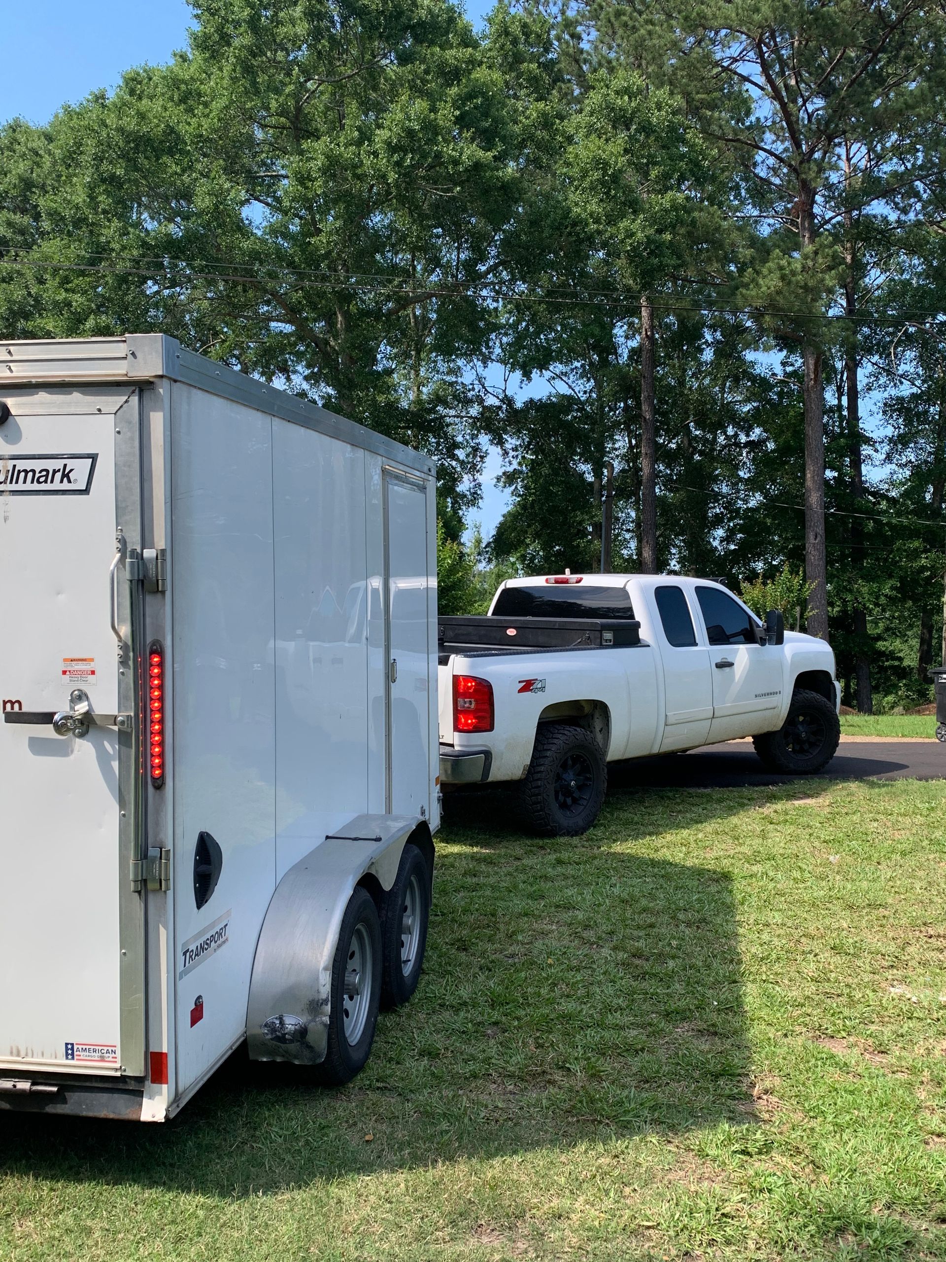A white truck is towing a white trailer in a grassy field.