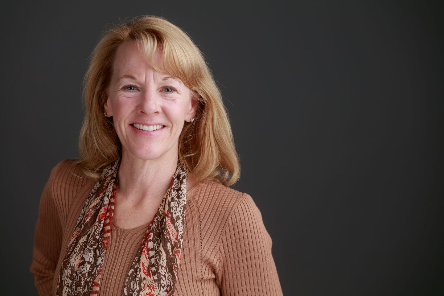 A woman in a brown sweater and scarf is smiling for the camera.