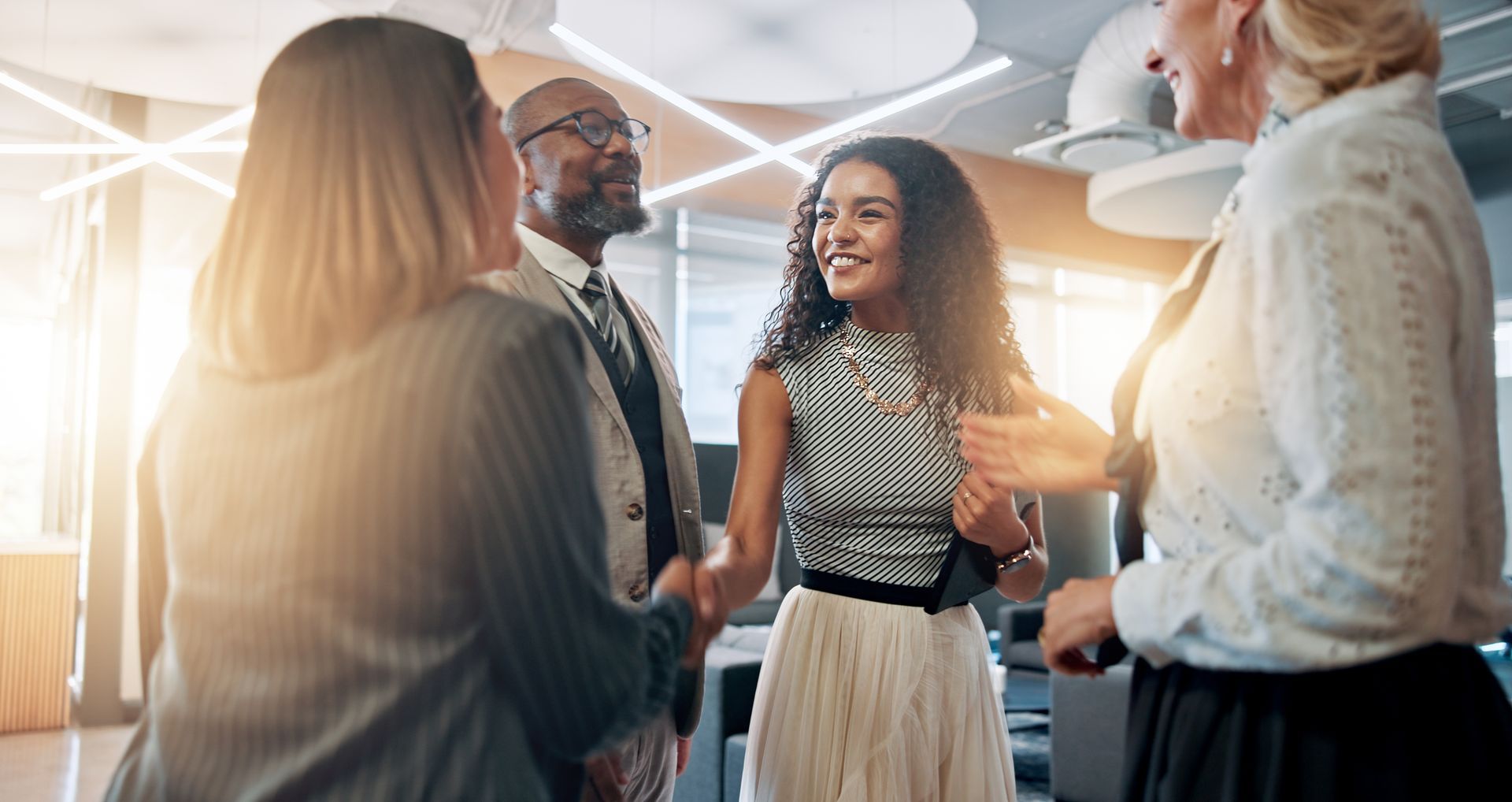 Businesspeople greet each other in an office. A woman shakes hands. Bright lighting.