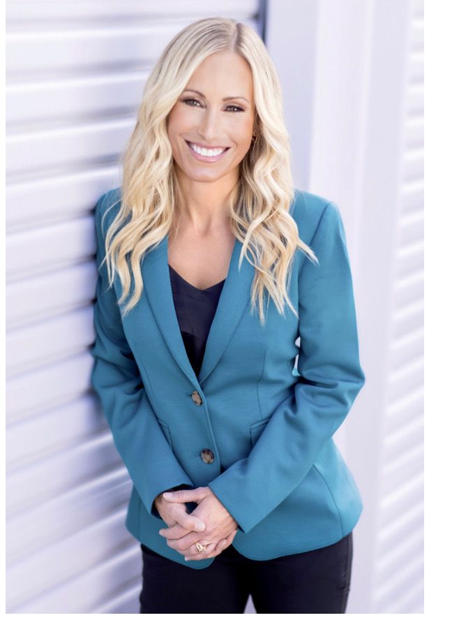 A woman in a blue jacket is standing in front of a wall.