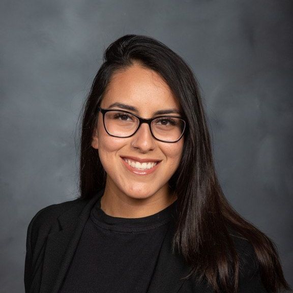 A woman wearing glasses and a black jacket is smiling for the camera.