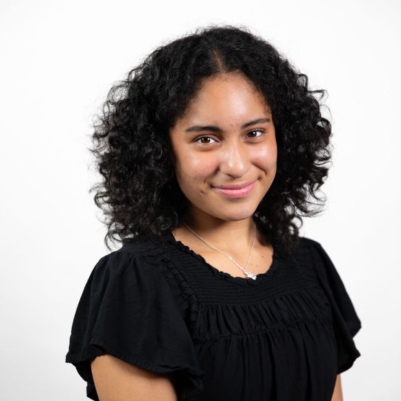 A woman with curly hair is wearing a black shirt and smiling.