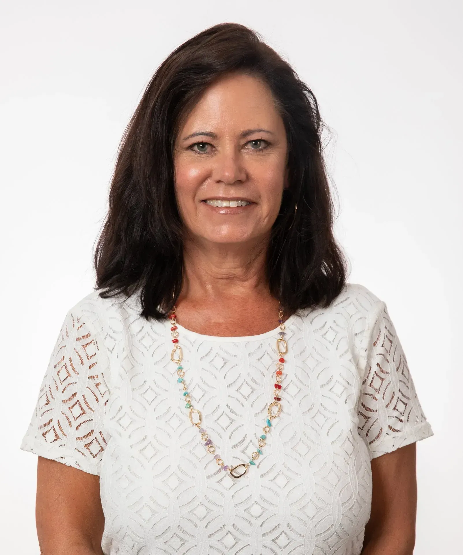 A woman wearing a white shirt and a necklace is smiling for the camera.