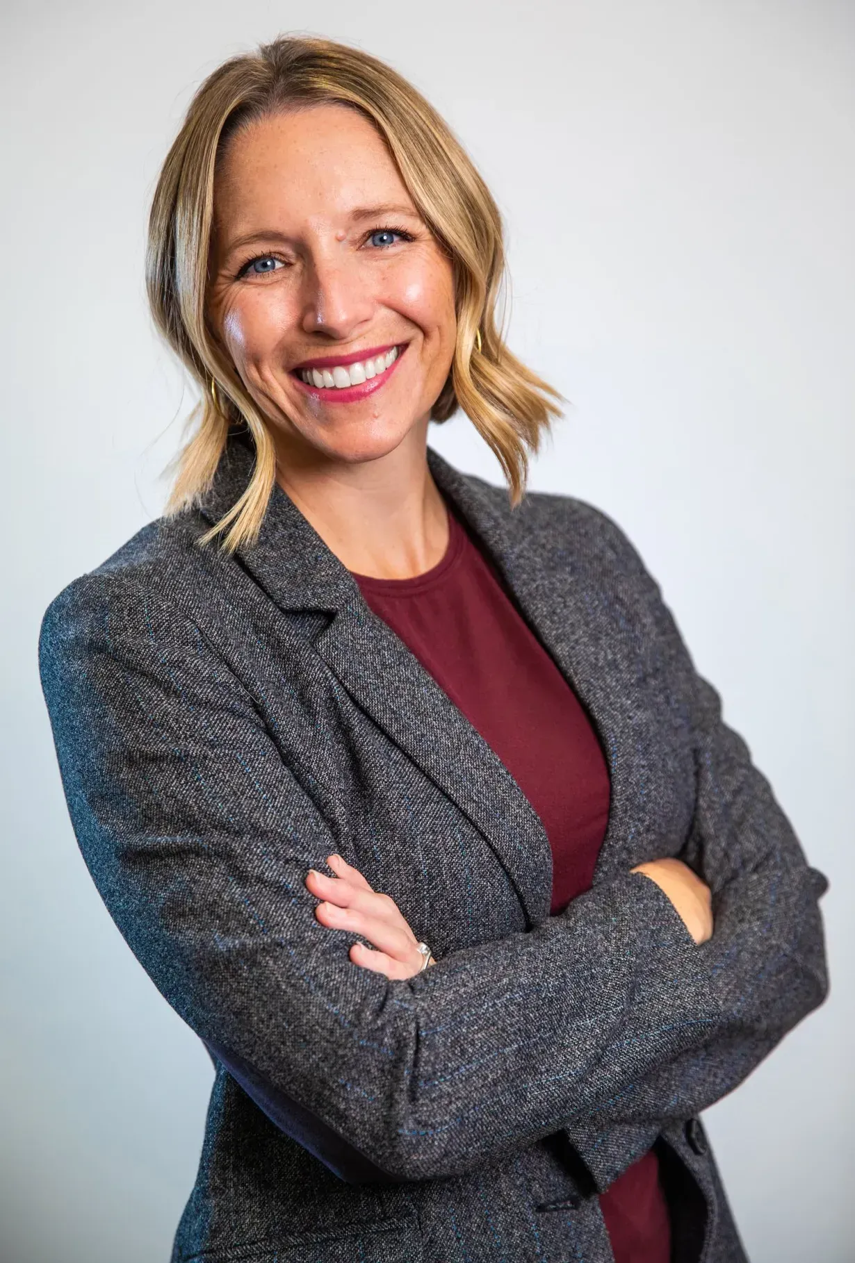 A woman in a suit is smiling with her arms crossed.
