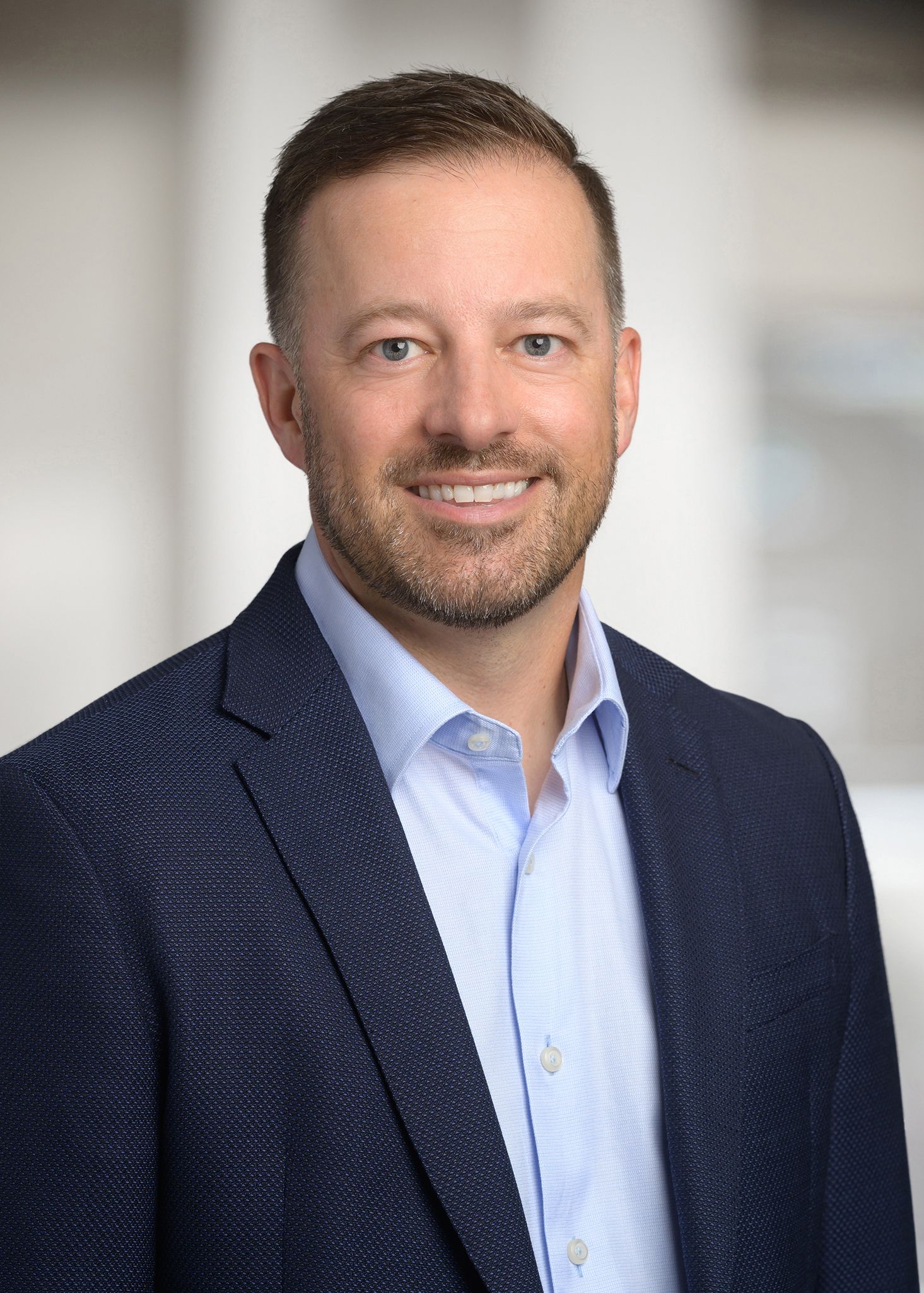A man in a suit and blue shirt is smiling for the camera.