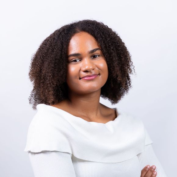 A woman with curly hair is wearing a white sweater and smiling.