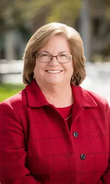 A woman wearing glasses and a red jacket is smiling for the camera.