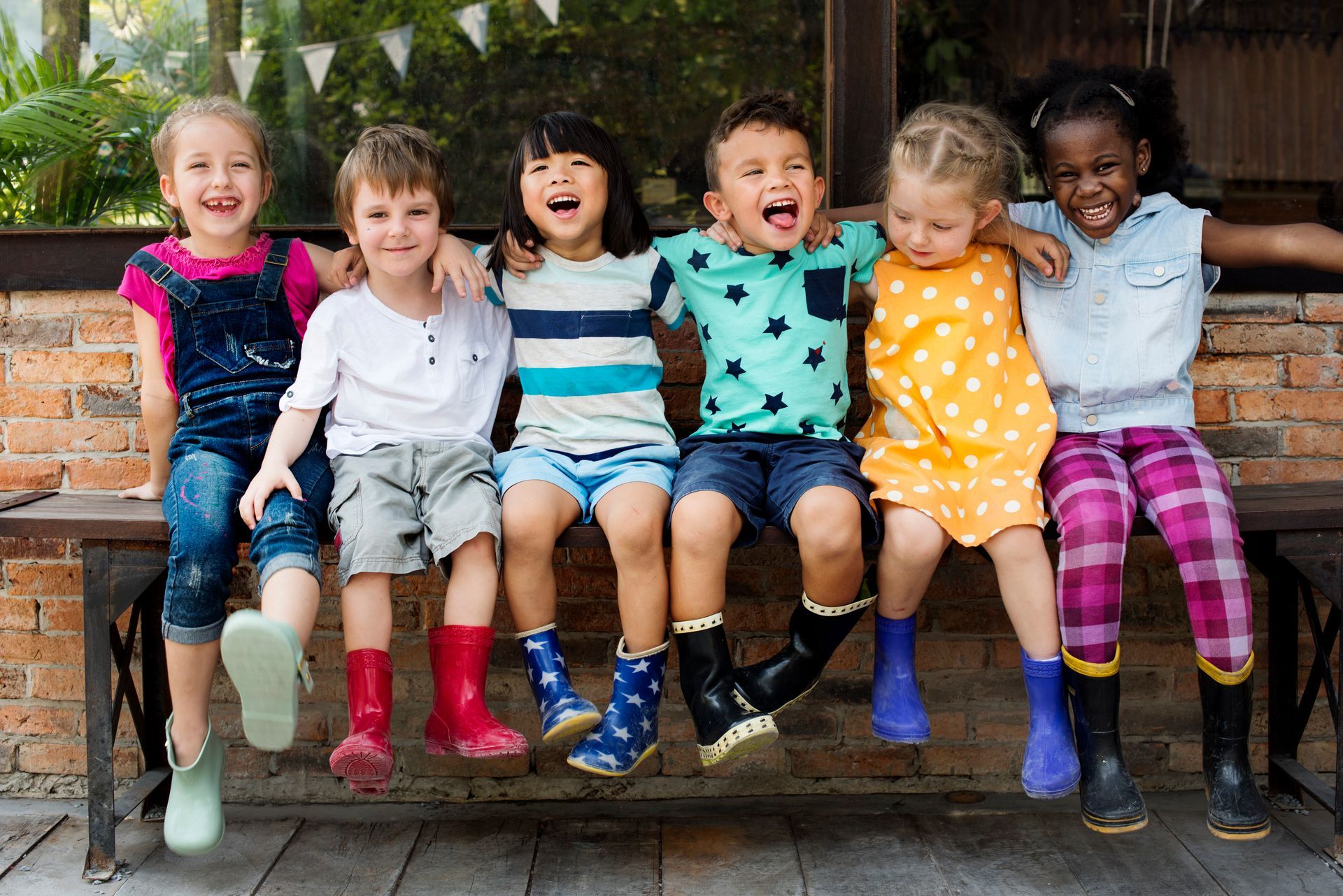 Children sitting on a bench, smiling and laughing, wearing colorful clothes and boots.