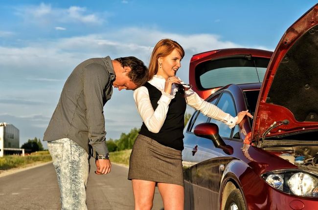 A man and a woman are looking under the hood of a car.