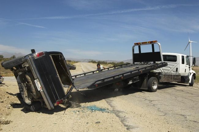 A tow truck is towing a car that has turned over on the side of the road.