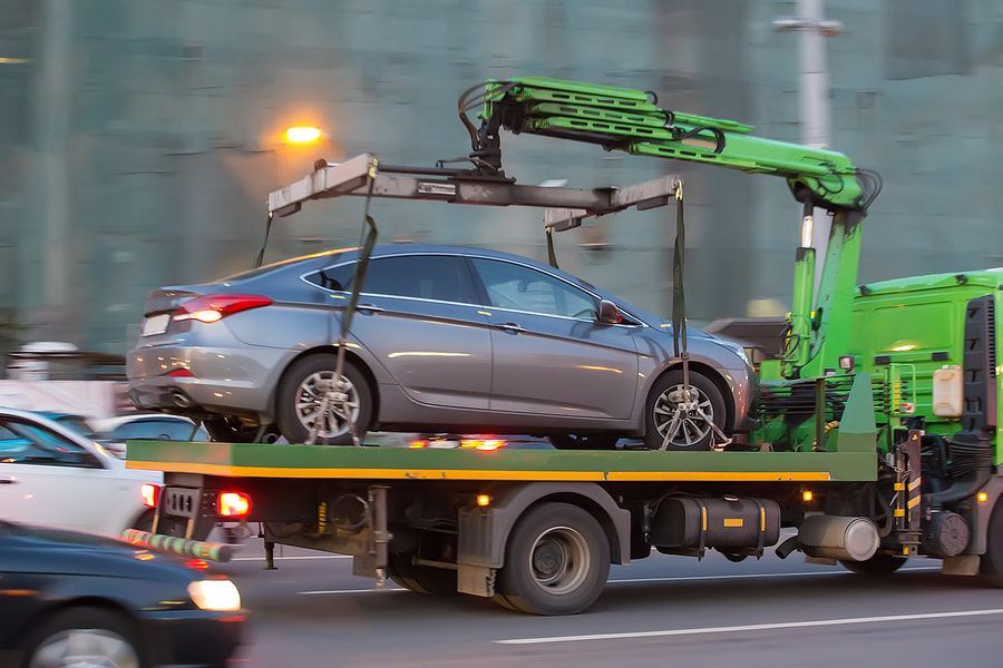 A car is being towed by a tow truck on a city street.