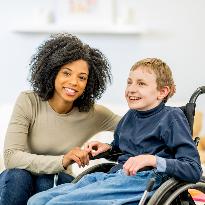Smiling person seated next to person in a wheelchair, indoors. They both appear happy.