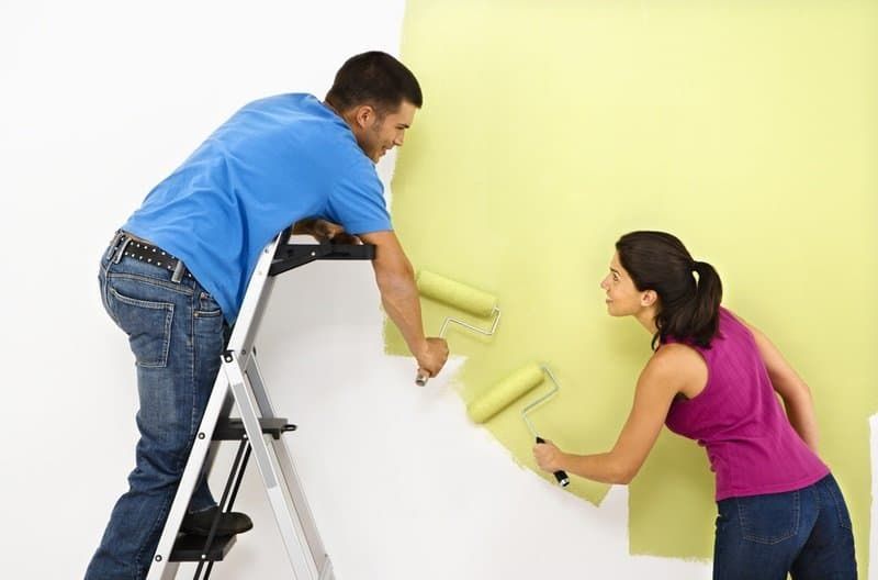 The Guy on the ladder and the girl is rolling the wall with yellow paint.