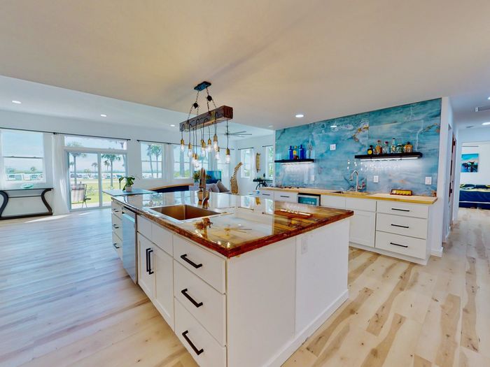 Modern white kitchen with a large island, wooden countertops, and a striking blue, marble-patterned backsplash wall.