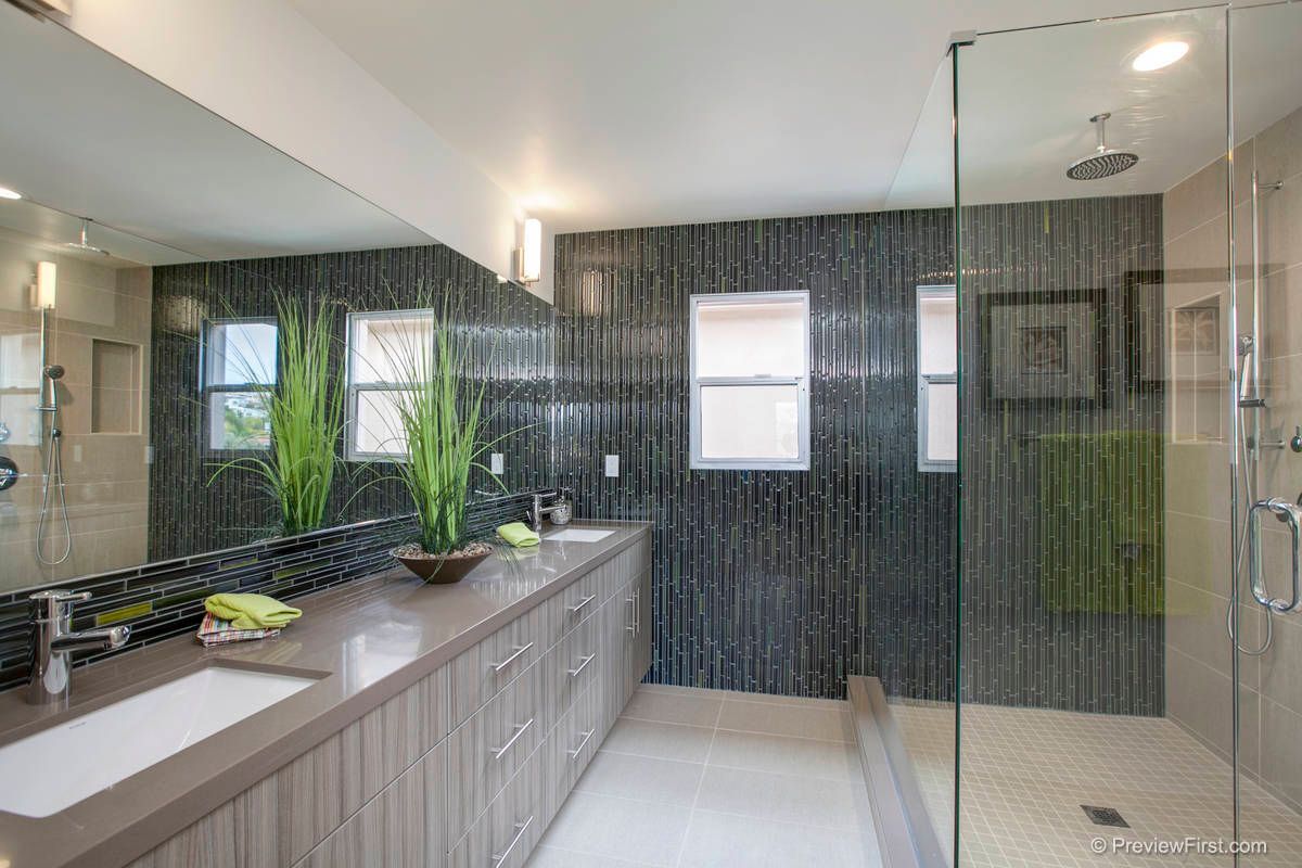 A modern bathroom with a long wood vanity, large mirror, dark tiled accent wall, and a walk-in glass shower.
