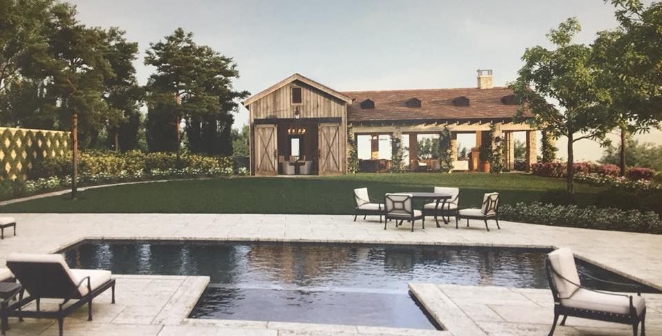 A rustic farmhouse with a lawn, swimming pool, and patio furniture on a sunny day.