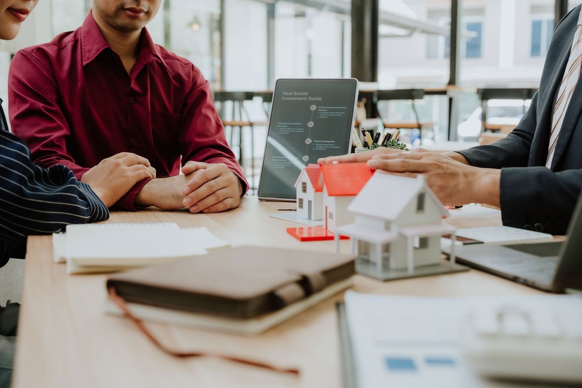 A professional in a suit discusses property models with clients at a desk in a bright office.