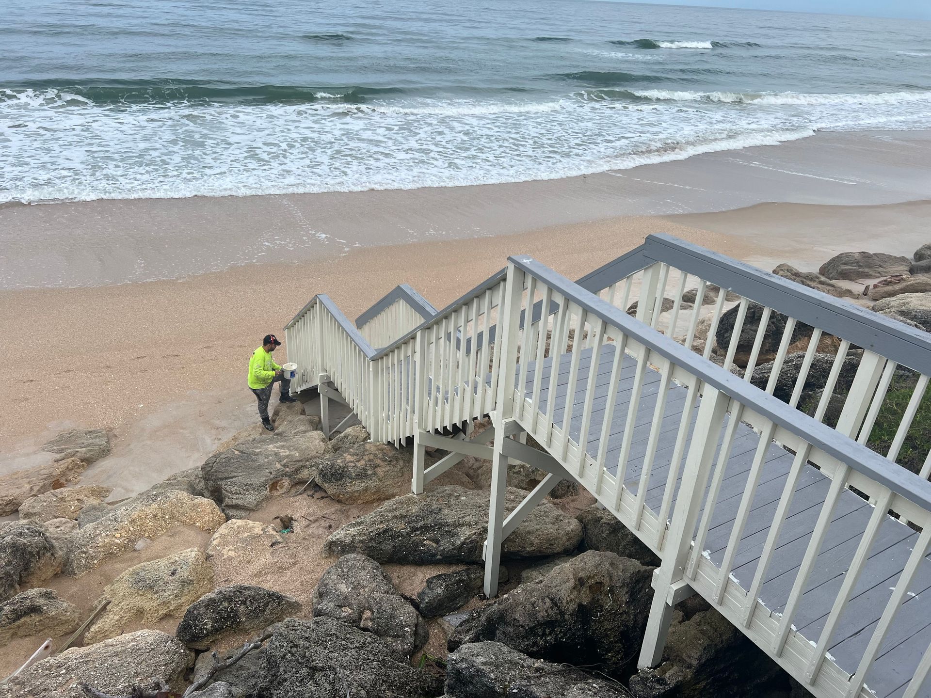 A man is sitting on the stairs leading to the beach.