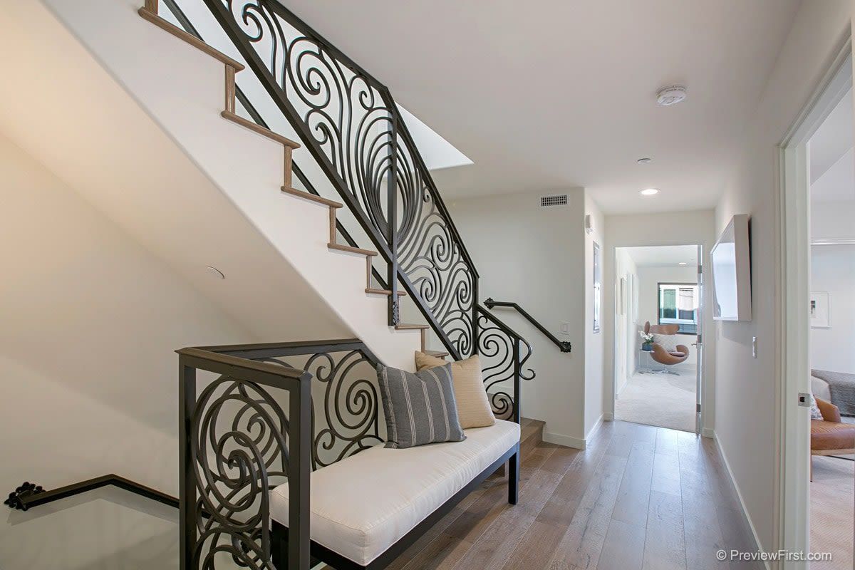 A staircase with a wrought iron railing and a bench in a hallway.