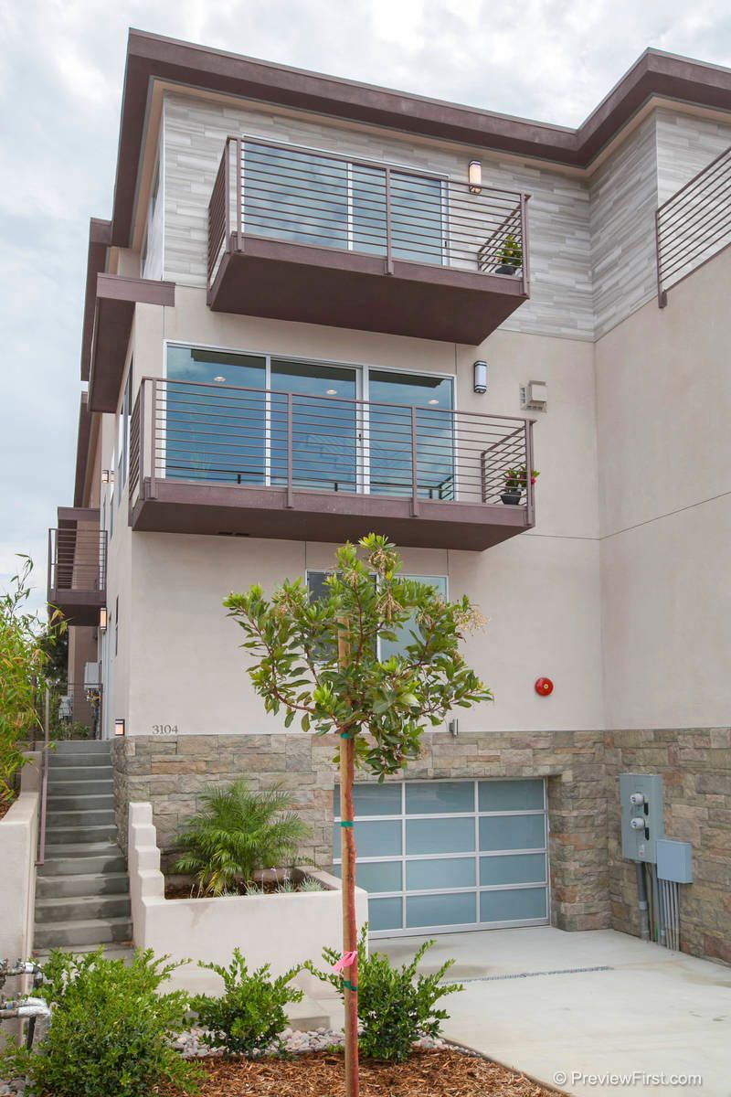 A house with a balcony and stairs and a tree in front of it.