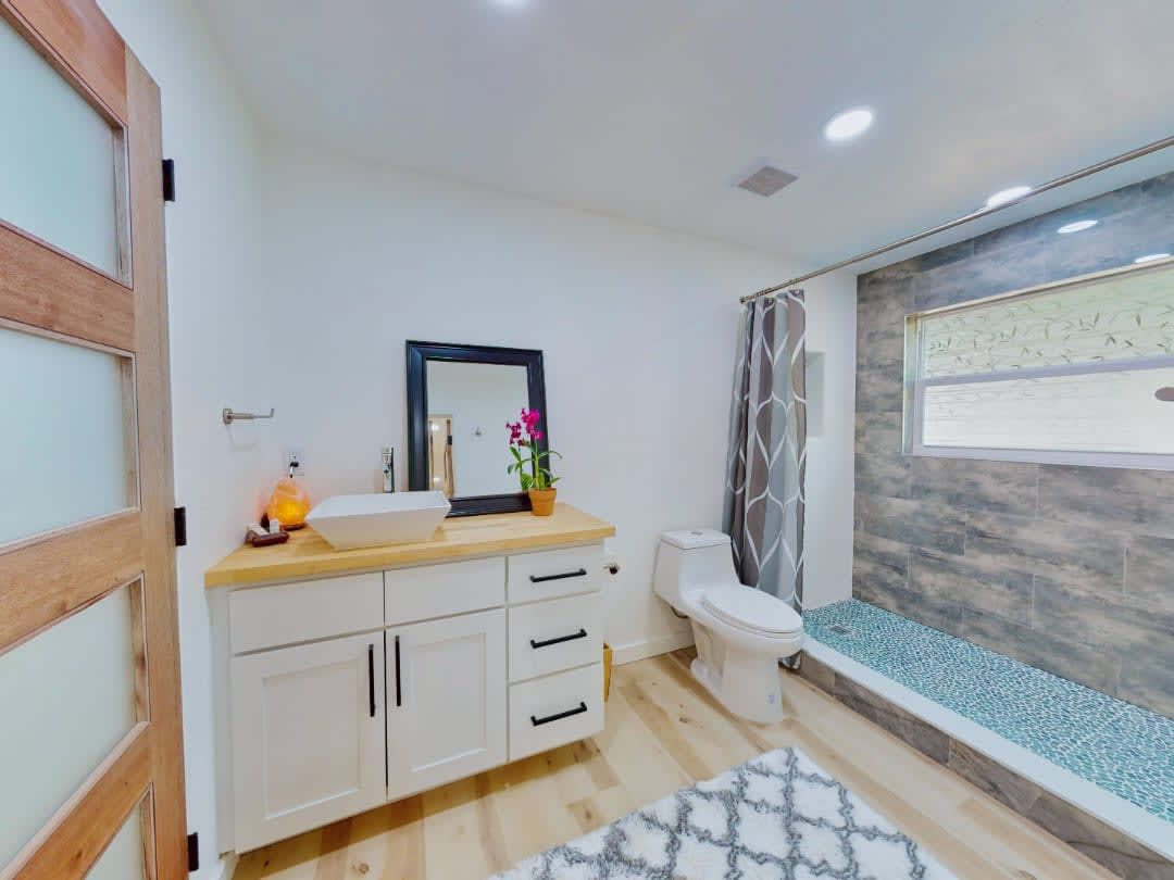 A bathroom with a toilet, sink, mirror and shower.