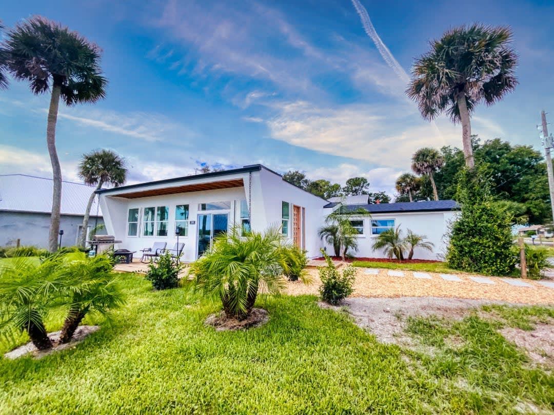 A white house with palm trees in front of it is for sale.