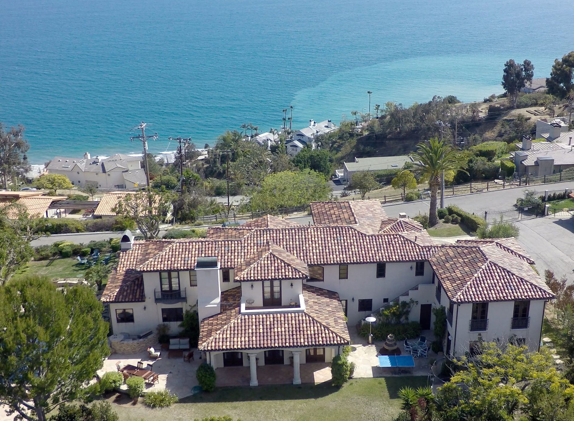 An aerial view of a large house on a hill overlooking the ocean.