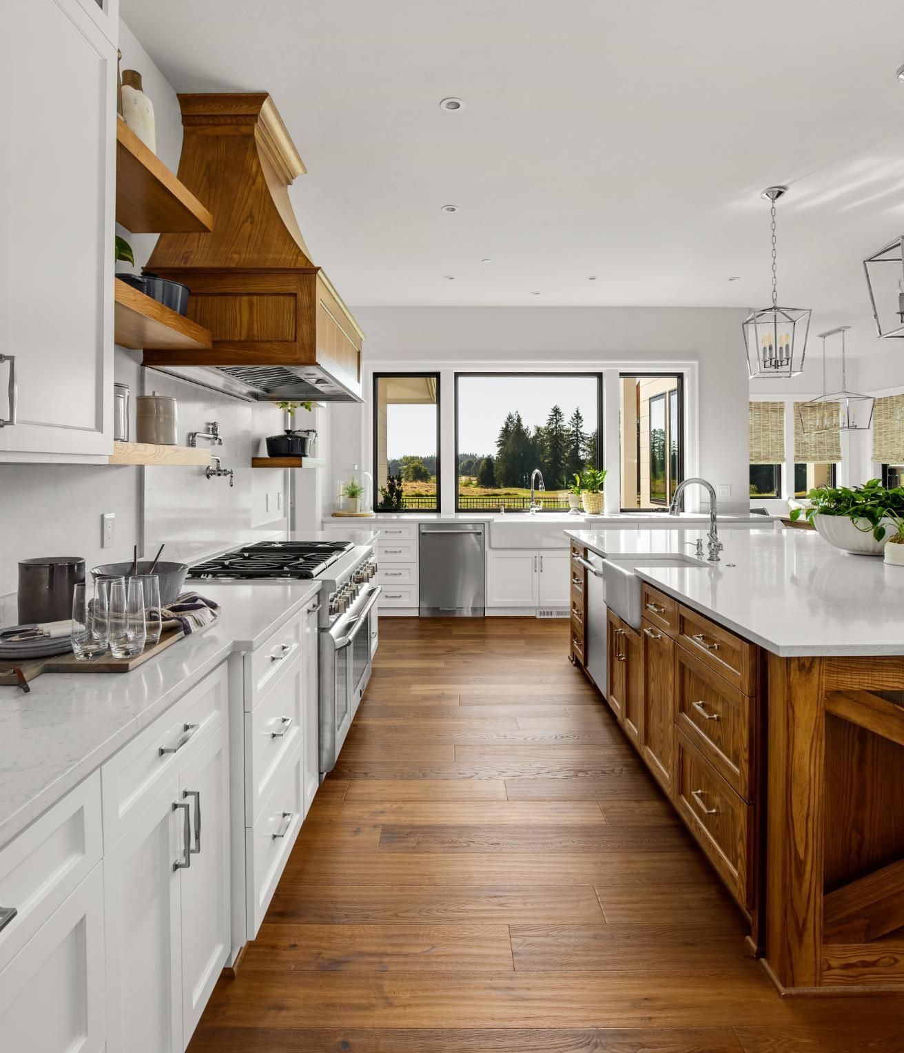 A bright kitchen with white cabinets, a wooden range hood, a kitchen island, stainless appliances, and a large window.