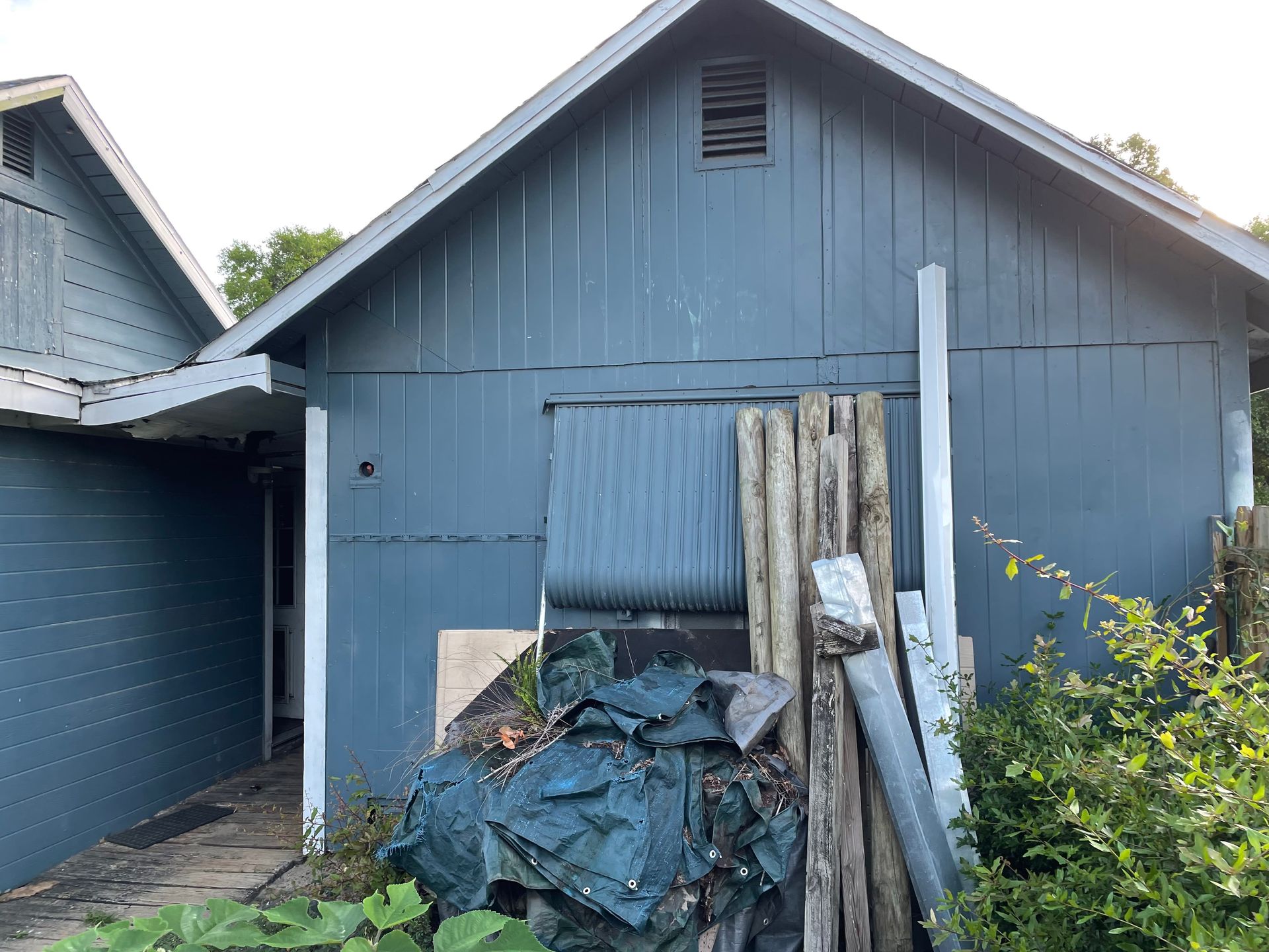 A blue house with a lot of wood in front of it.