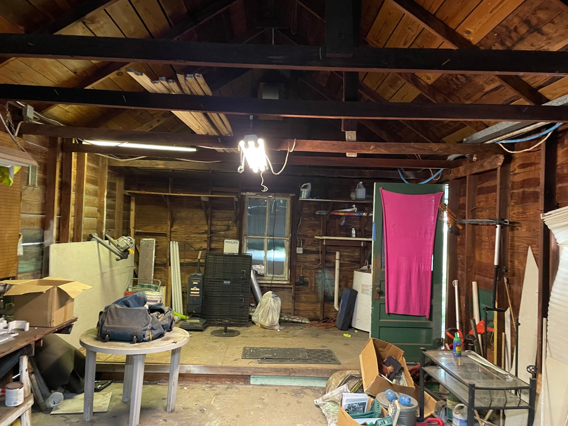 A room with a wooden ceiling and a pink shirt hanging on the wall.