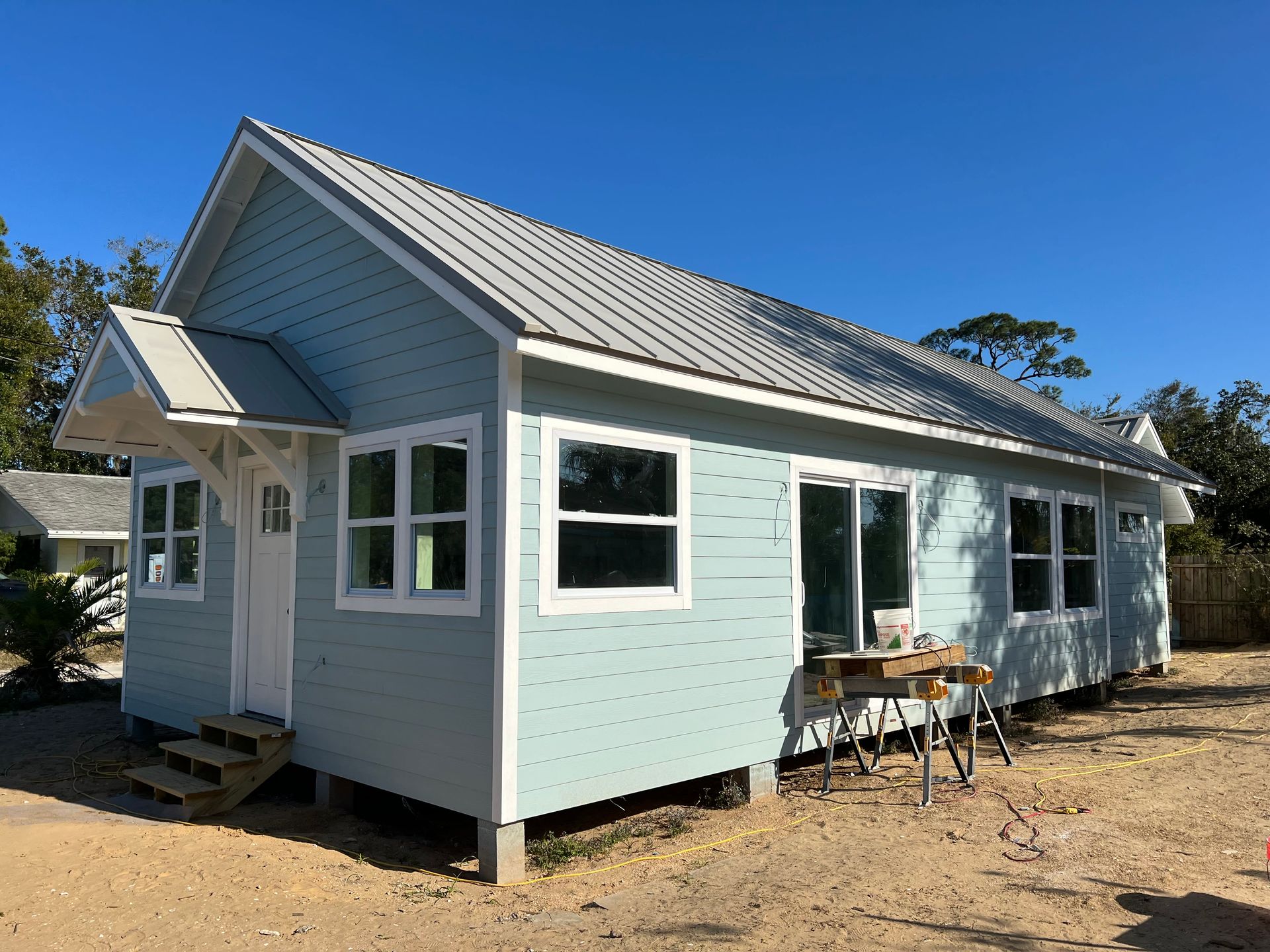 A small house with a metal roof is sitting in the middle of a dirt field.