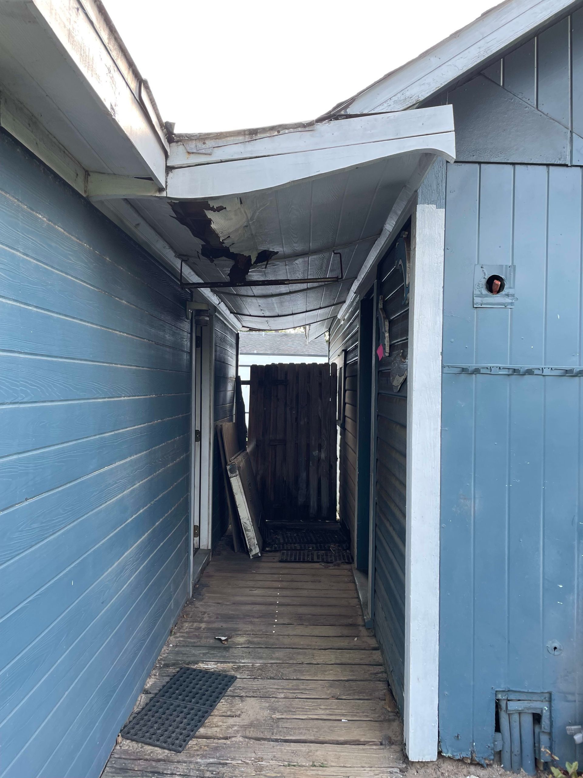 A narrow hallway between two blue houses with a wooden floor.